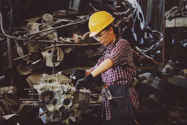 seguro de vida para trabajadores: Empleado cortando con una cierra el metal dentro de una obscura fabrica.